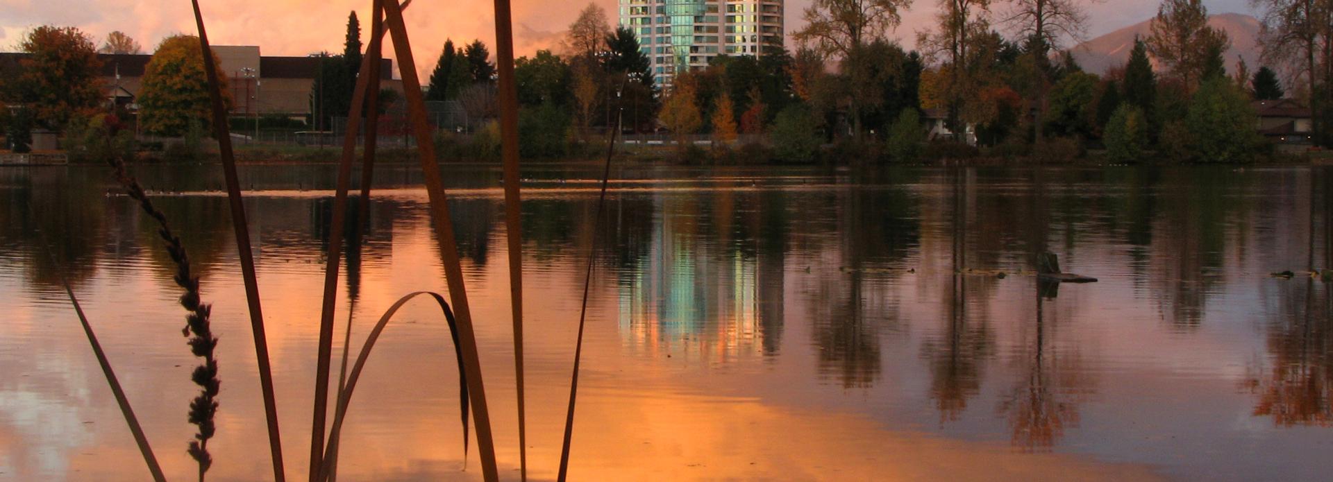 Lake reflecting an orange sunrise-lit sky, with fall trees and buildings on the other side of the lake