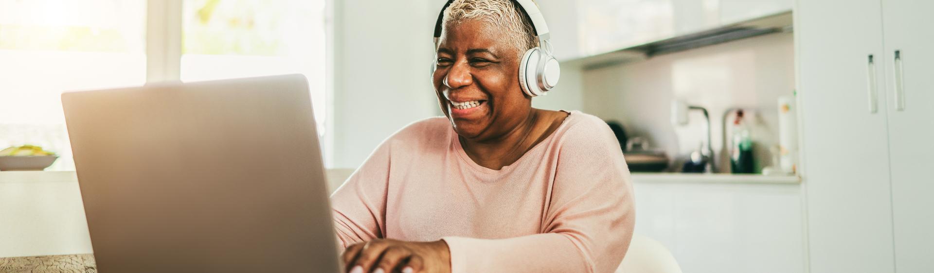 A senior woman using a laptop while wearing headphones.