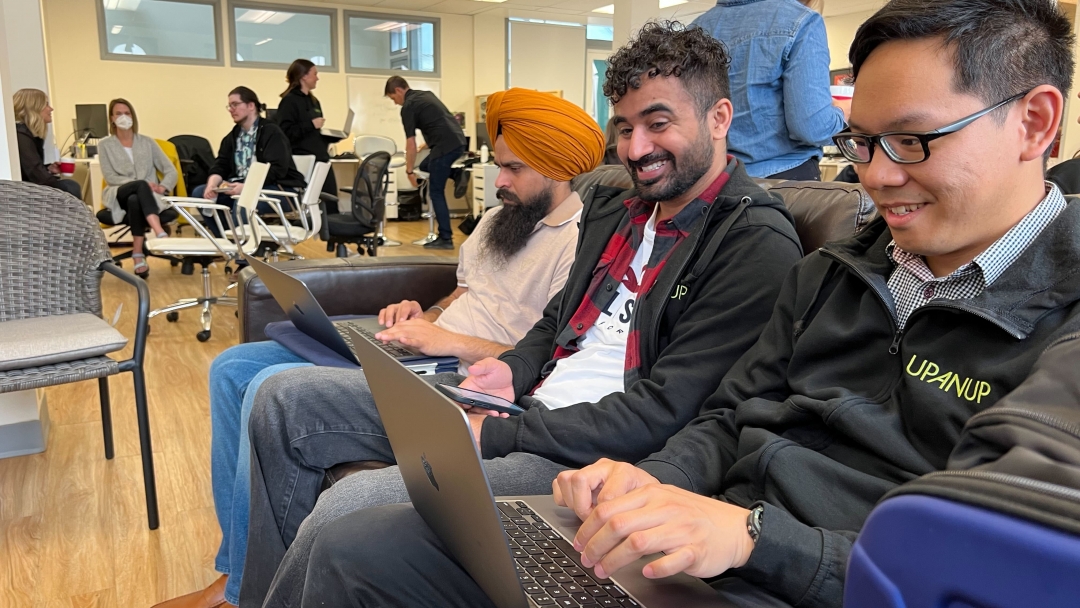 Three men sitting on a couch with laptops. 