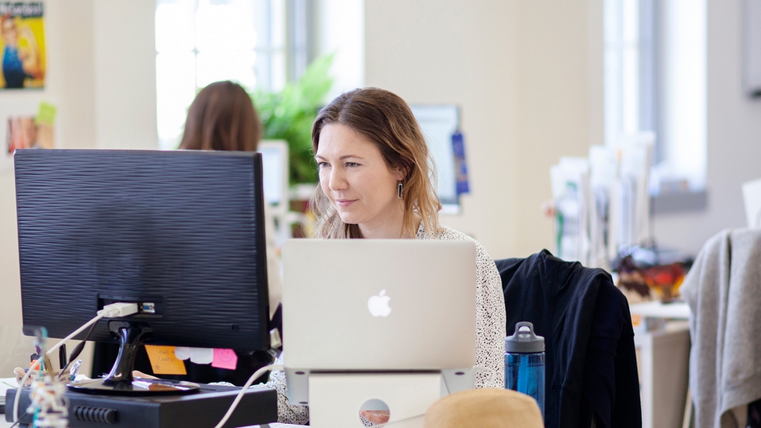 Woman sitting at a desk in an office and looking at a screen. 