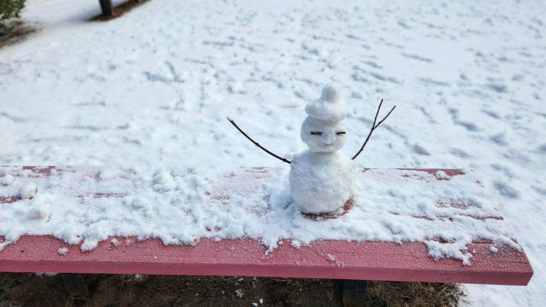 Small snowman on a red bench surrounded by snow