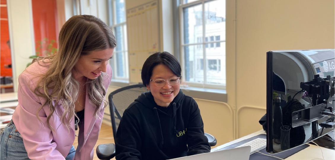 Two women by a desk looking at computer screens. 