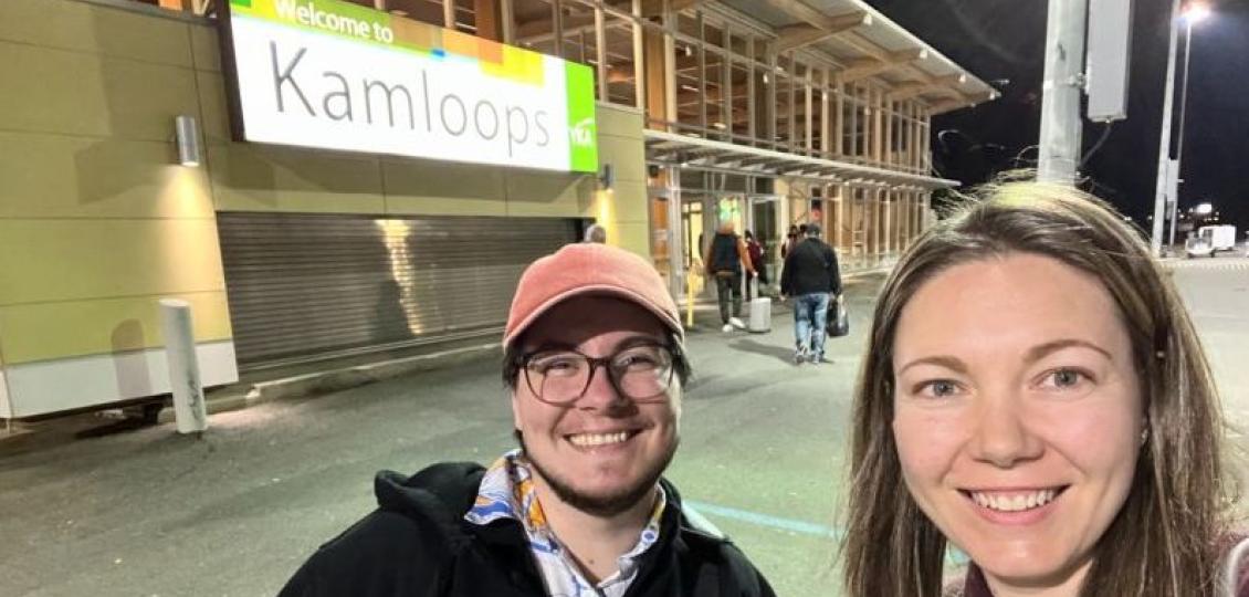 Two people taking a selfie smiling in front of the welcome to kamloops building sign.