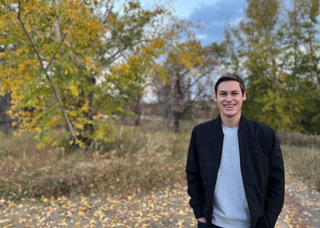 Man standing outside near trees in a dark blue jacket. 