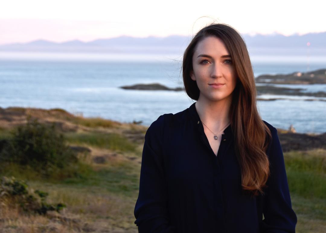A front facing portrait view of Sophie in a black top with the sea behind her.