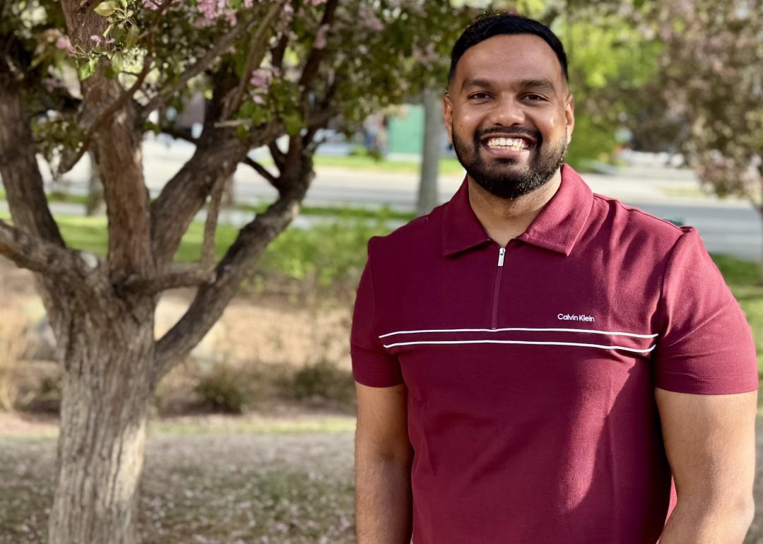 Front facing profile photo of male smiling on the right hand side, with a tree in the background on the left side
