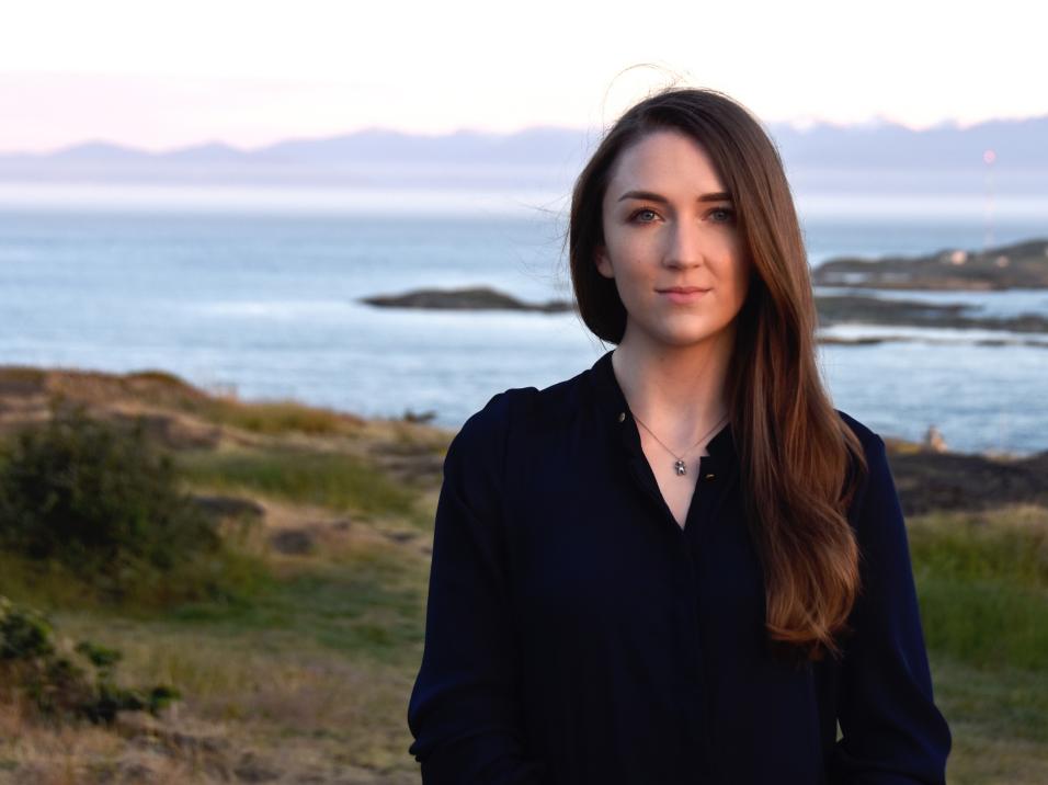 A front facing portrait view of Sophie in a black top with the sea behind her.