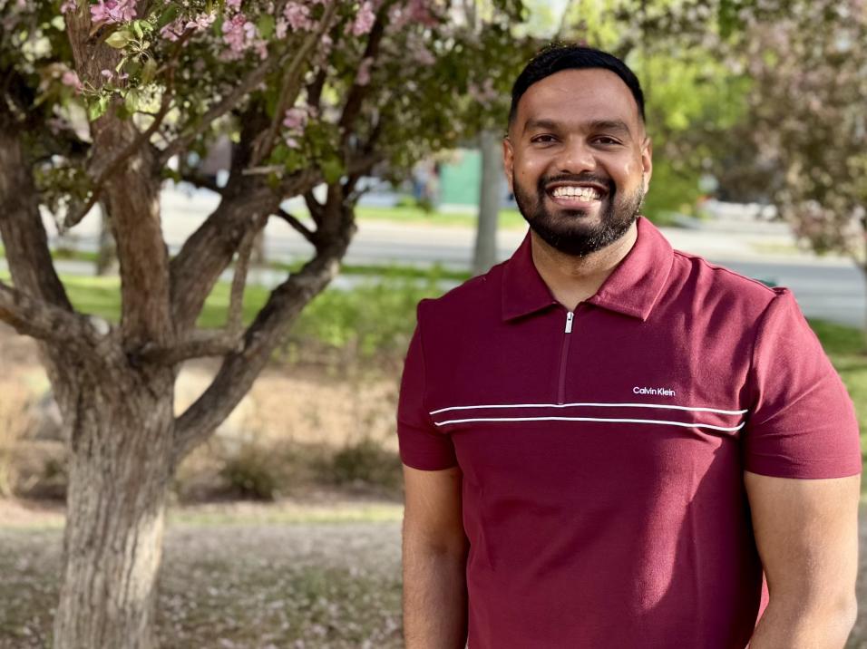 Front facing profile photo of male smiling on the right hand side, with a tree in the background on the left side